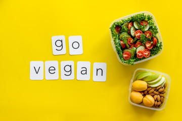 to-go box with salad, nuts, fruit and go vegan text for vegetarian lunch on yellow background top view