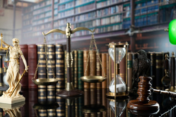 The law concept background.  White statue of Themis, gavel, legal books, scale and the hourglas on the table in the old court library.