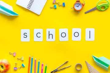 Education concept with school word and frame of stationery with notebook, pens, clock on yellow background top view