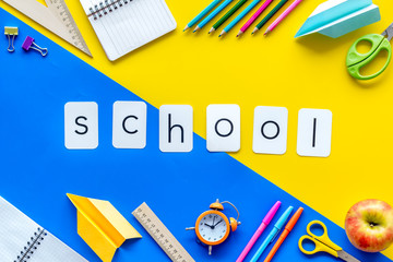 Education with school word and frame of stationery with notebook, pens, clock on yellow and blue background top view