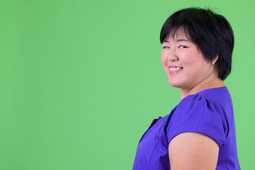 Closeup profile view of young happy overweight Asian woman looking at camera