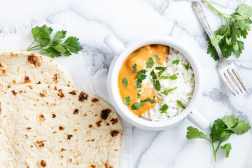 Top view of Indian butter chicken with jasmine rice, fresh baked naan, topped with cilantro, marble background