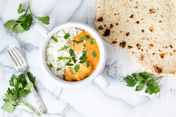Top view of Indian butter chicken with jasmine rice, fresh baked naan, topped with cilantro, marble background