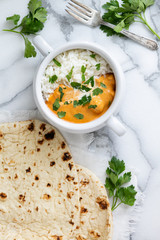 Top view of Indian butter chicken with jasmine rice, fresh baked naan, topped with cilantro, marble background