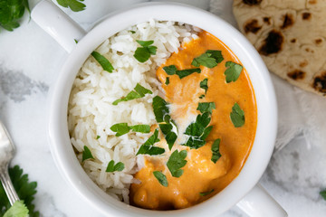 Top view of Indian butter chicken with jasmine rice, fresh baked naan, topped with cilantro, marble background