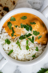 Top view of Indian butter chicken with jasmine rice, fresh baked naan, topped with cilantro, marble background