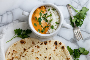 Top view of Indian butter chicken with jasmine rice, fresh baked naan, topped with cilantro, marble background