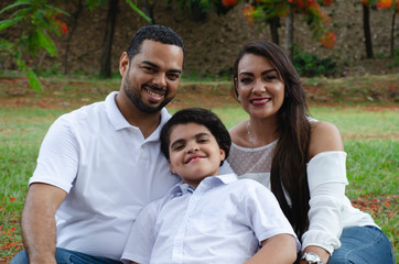 Obraz premium couple of Latin American men and women, with boy suffers autism, happy in a portrait family outdoors together in a park, the three laughing hugging