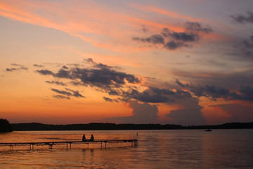 Beautiful summer landscape with colorful after sunset sky.Scenic view with bright color sky reflects in a lake and two silhouettes on a wooden pier enjoying sunset over lake Mendota. Madison, WI, USA.