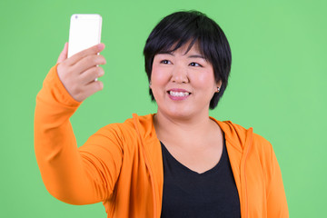 Young happy overweight Asian woman taking selfie ready for gym