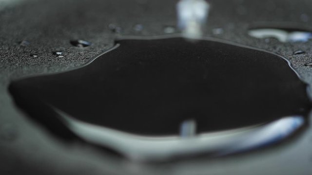 Water drop capture in slow motion on close up macro camera when it hit vodn&iacute; hladinu a pomalu se rozpust&iacute; do stran on dark backgound plate with light reflection.