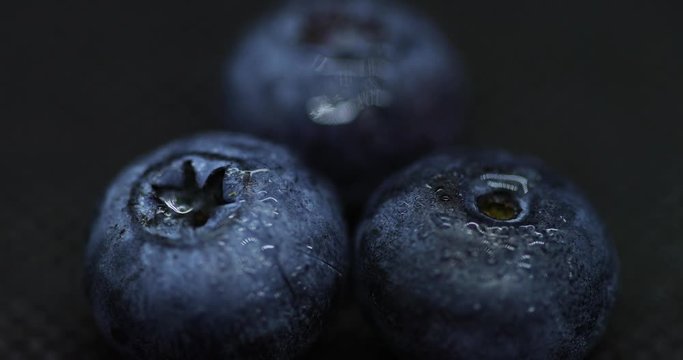 Close up macro shot of blueberries laying on dark splashed and spayed water background captured water drops in slow motion.