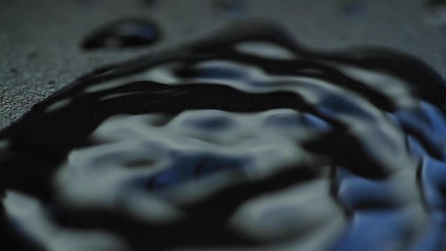 Water drop capture in slow motion on close up macro camera when it hit vodn&iacute; hladinu a pomalu se rozpust&iacute; do stran on dark backgound plate with light reflection.