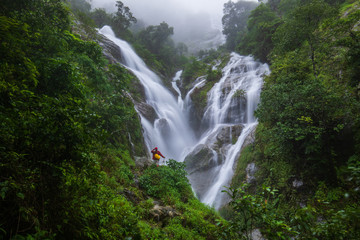 Fototapeta premium The girl in red sweater touring on Pi-tu-gro waterfall, Beautiful waterfall in Tak province, ThaiLand.