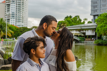 Fototapeta premium couple of Latin American men and women, with boy suffers autism, happy in a portrait family outdoors together in a park, the three laughing hugging