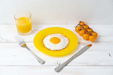 fried egg on yellow plate with orange juice and cherry tomatoes on white wooden table. Fresh breakfast.