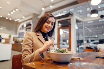 Girl eats vegetable salad. Lady sitting in a cafe. Brunette in a brown coat