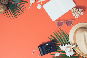 Colorful summer holidays fashion flat lay - straw hat, camera, sunglasses, sea shells on bright orange background