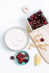 White chilled gazpacho soup with oil drizzle and cherry, lemon, and marcona almond ingredients on wood cutting board / overhead view isolated on white background
