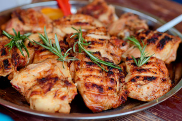 The chicken thighs fried on a barbecue close up, with rosemary branches on a tray.