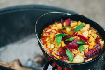 Vegetarian red and golden beet stew with potatoes and seasoned with fresh herbs cooking in cast iron dutch oven on campfire grill