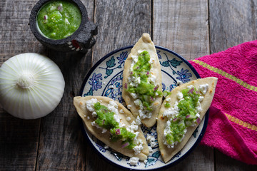 Mexican tlacoyos with green sauce on wooden background