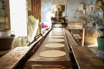 Las tortillas de maíz están saliendo en serie de la maquina antigua. - obrazy, fototapety, plakaty