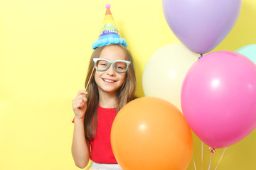 Fototapeta na wymiar Portrait of a little cute girl in a festive cap and with balloons on a colored background. Birthday, holiday.