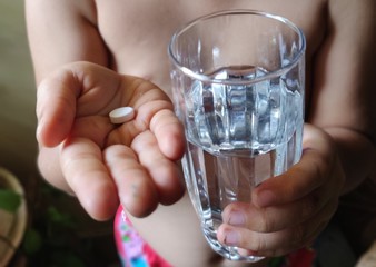 small kid holding a glass of water and medicine in sick day