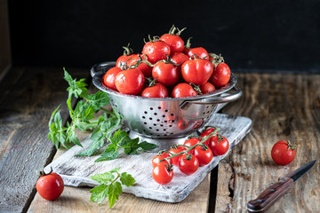 Group of red cherry tomatoes in a metal colander on a wooden table.