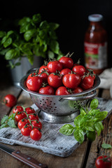 Group of red cherry tomatoes in a metal colander on a wooden table.