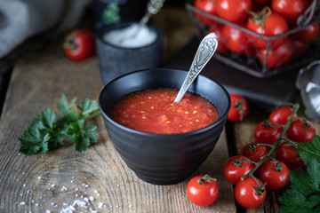 Group of red cherry tomatoes as an ingredient for tomato sauce in a black bowl on a wooden table.
