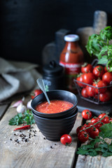 Group of red cherry tomatoes as an ingredient for tomato sauce in a black bowl on a wooden table.