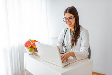 Young female nutritionist working in her office. Smiling nutritionist in her office, healthy vegetables and fruits, healthcare and diet concept. Smiling young dietician sitting at desk