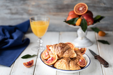 Breakfast croissants lie on a blue plate and red oranges on a white background. Orange juice