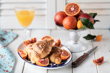 Breakfast croissants lie on a blue plate and red oranges on a white background. Orange juice