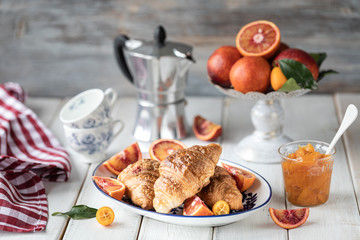 Breakfast croissants lie on a blue plate and red oranges on a white background. Orange juice. A cup of coffee