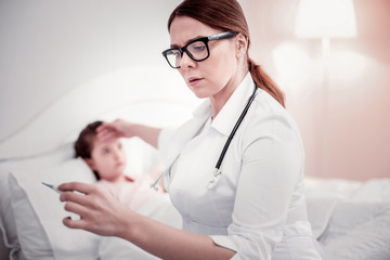 Obraz premium Serious professional doctor looking at the thermometer