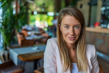 Closeup face of smiling woman sitting in cafeteria. Successful lady in a cafe pub. Portrait of woman smiling in coffee shop. Young smiling business woman sitting in cafe