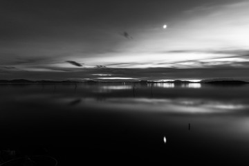 Moon above a lake with its reflection on the Trasimeno lake surface at dusk