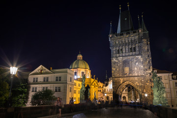 Obraz premium People at the Charles Bridge (Karluv most) and lit St. Francis of Assissi Church and Old Town Bridge Tower at the Old Town in Prague, Czech Republic, in the evening.