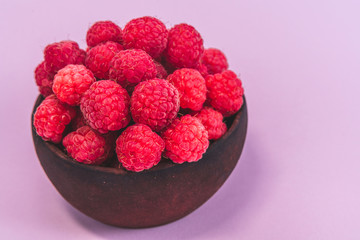 Fresh organic raspberries in a clay plate on pink background.