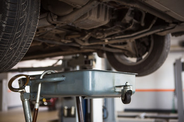 Car repair in the service station. Under the car on the lift substituted apparatus for draining oil and working off.