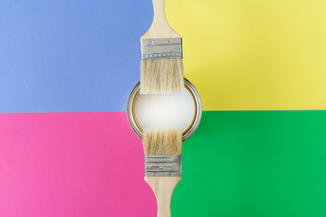 Brush with wooden handle and open can with white paint on colorful background. Renovation concept. Place for text.