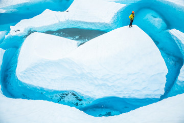 Stranded on a large ice fin, a man stands on top looking at the lake surrounding him.