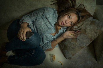 portrait of young attractive depressed and helpless addict woman feeling desperate sad abusing pills and tablets dumped via mobile phone - obrazy, fototapety, plakaty