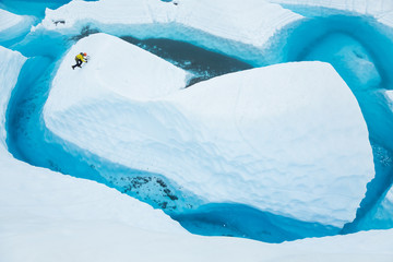 Ice climber soloing up an island of ice that looks like an iceberg in a large blue pool on the Matanuska Glacier.