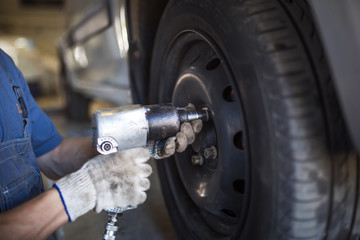 Car repair in the service station. Hands of a mechanic in overalls repairing the car on the lift without wheel, holding the tire and mechanical works.