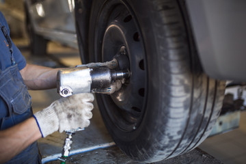 Car repair in the service station. Hands of a mechanic in overalls repairing the car on the lift without wheel, holding the tire and mechanical works.