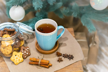 Winter theme. Christmas tea with spices, cup of tea with cinnamon, anise, cookies in a shape of star on wooden background linen napkin. Mug of tea with Christmas decoration. Copy space for text